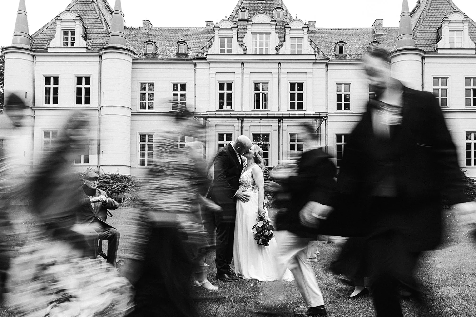 Hochzeitsfotograf Potsdam Das Brautpaar beim Küssen und die Gäste laufen durchs Bild